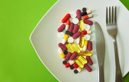 Dieting gone too far. Studio shot of medication served on a plate with a fork and knife against a green background.の写真素材