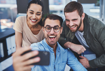 We have fun while working hard. a group of designers taking selfies together in an office.の写真素材