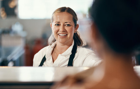 A friendly smile speaks volumes. a mature barista serving a customer at a cafe.の写真素材