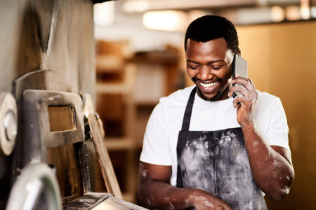 Ill make your lunchtime real special with a fresh delivery. a male baker using his cellphone while working.の写真素材