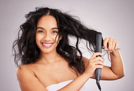 Portrait, happy woman and hair straightener for beauty in studio, treatment and wellness on background. Female model, haircare and heat styling equipment for ironing curly hairstyle, texture or toolsの写真素材
