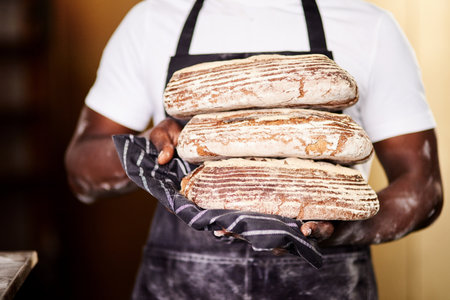 They are fresh and delicious. a male baker holding freshly baked bread in his bakery.の写真素材