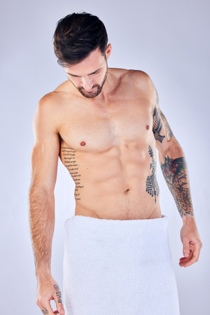 Body, health and man in towel in studio after shower, cleaning or bathing for hygiene and wellness isolated on a gray background. Topless, body art and male fitness model with tattoos, abs and muscleの写真素材