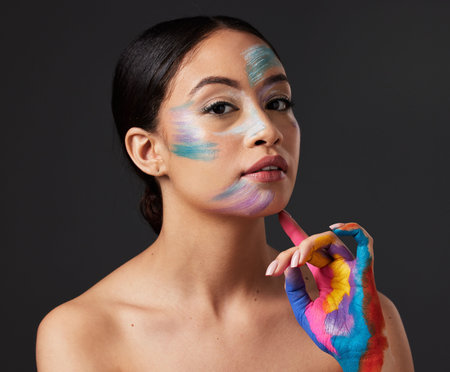 Woman, beauty and portrait with rainbow hand paint art on face in studio with glow. Creative skin and makeup on female aesthetic model serious on gray background for lgbtq color inspiration on handsの写真素材