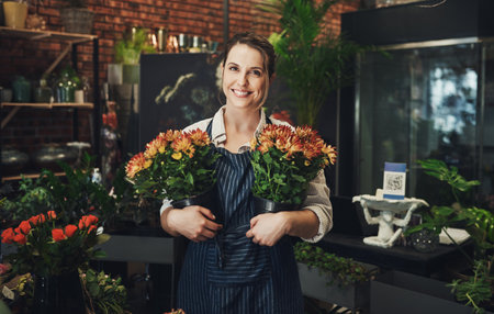 Flowers make life a little lovelier. Portrait of an attractive young florist holding potted flowers inside a pant nursery.の写真素材