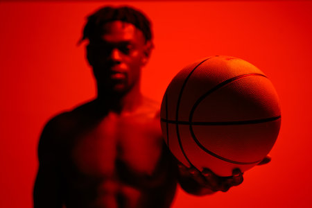 Im doing it for the love of the game. Red filtered shot of a young sportsman posing with a basketball in the studio.の写真素材