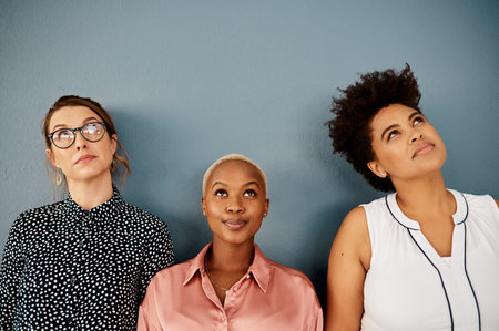 Is everybody thinking what Im thinking. Studio shot of a group of three attractive young businesswomen looking thoughtful while standing against a grey background.の写真素材