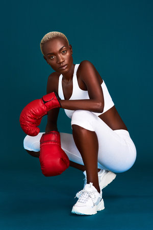 Confidence radiates off of her. Full length portrait of an attractive young female boxer crouching against a dark background with her boxing gloves on.の写真素材
