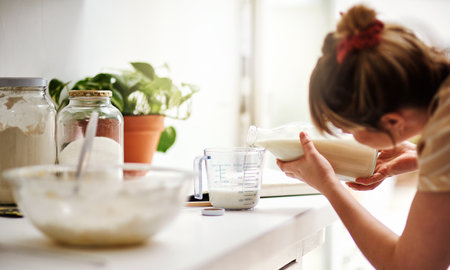 Baking is a science. a young woman measuring milk while baking at home.の写真素材
