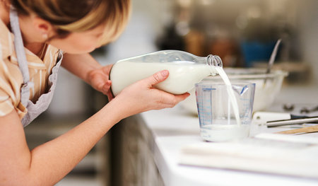 Make sure you get the correct measurements. a young woman measuring milk while baking at home.の写真素材