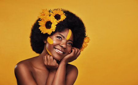 Flowers make a woman as happy as a lark. Studio shot of a beautiful young woman smiling while posing with sunflowers in her hair against a mustard background.の写真素材