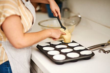 One spoonful is more than enough. an unrecognizable woman spooning batter into a muffin pan.の写真素材