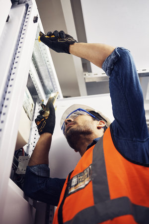 Engineer, electrician and maintenance man with screwdriver in control room for power box. Male technician person for inspection service for engineering, electricity or energy supply repair with torchの写真素材
