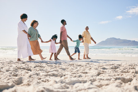 Holding hands, vacation and family on beach, walking and break to relax, happiness and ocean water waves. Grandparents, father and mother with grandkids, seaside holiday and quality time togetherの写真素材