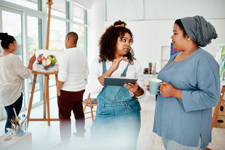 Can I get your opinion on this. two attractive women standing together and using a tablet during an art class.の写真素材