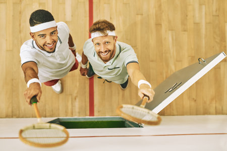 Once a squash player, always a squash player. High angle shot of two young men holding up their rackets at a squash court.の写真素材
