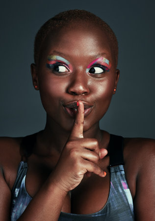 If only they knew the truth. a beautiful young woman posing with her finger on her lips against a grey background.の写真素材