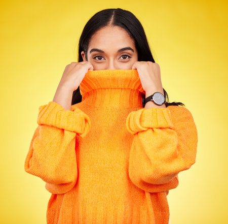 Cold, cover and portrait of a woman with a jersey isolated on a yellow background in a studio. Hiding, winter and a girl holding a jumper up for covering, warmth and bad weather on a backdropの写真素材