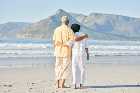 Old couple at beach, hug and travel with retirement and love outdoor, vacation with ocean view and relax in nature. Peace, zen and tropical island, man and woman watching sea waves, back and wellnessの写真素材
