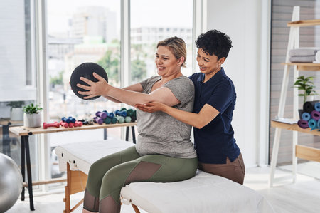 Were both not dropping the ball anytime soon. a young physiotherapist helping her mature patient exercise with a medicine ball inside her office at a clinic.の写真素材
