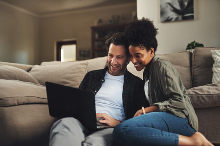 Were both loving this website. a happy young couple using a laptop while relaxing on a couch in their living room at home.の写真素材