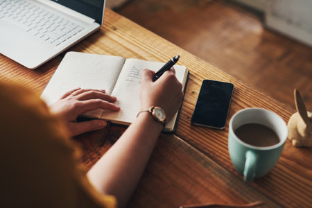 Get organised, get it done. an unrecognisable woman writing in a notebook while working from home.の写真素材