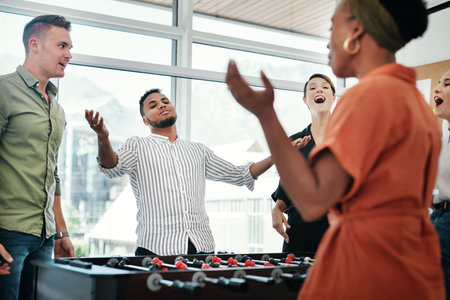 That was so close. a diverse group of businesspeople standing together and bonding over a game of foosball in the office.の写真素材