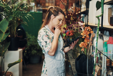 Is this correct. an attractive young businesswoman standing alone in her floristry and looking contemplative while using a tablet.の写真素材