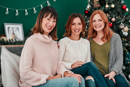 We still believe in Santa. Portrait of three attractive women sitting on the sofa at Christmas time together at home.の写真素材