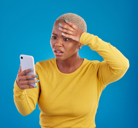 Wtf, phone and confused black woman in studio for fake news, social media and text on blue background. Omg, scam and girl with smartphone notification for phishing alert, glitch or internet problemの写真素材