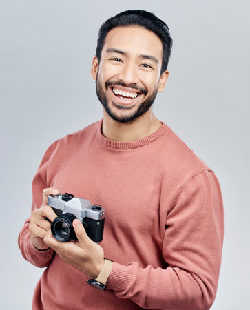 Portrait, studio and man with camera, tourist and photographer against a grey background. Face, male creative and guy with smile, photography and artist with happiness, memories and capture momentの写真素材