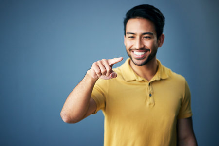 Mockup, smile and Asian man pointing, space and product placement against blue studio background. Japan, male and happy guy with brand development, happiness and suggestion with promotion and choiceの写真素材