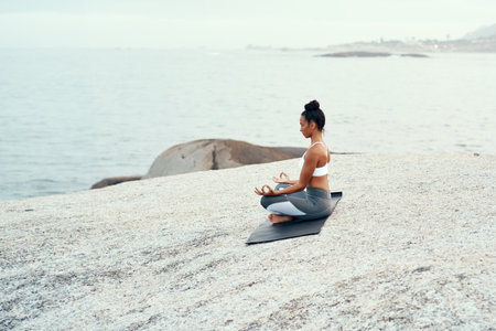 Find your way to freedom through yoga. a sporty young woman practicing yoga at the beach.の写真素材