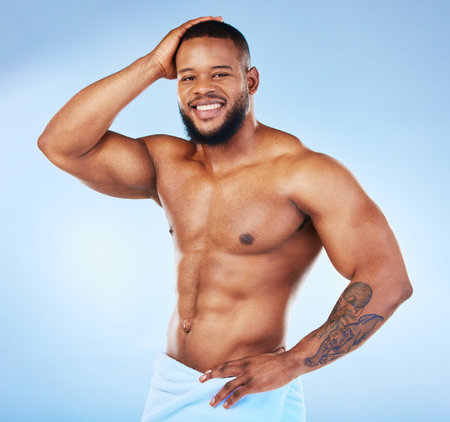 Towel, shower and fitness portrait of a black man with happiness from bodybuilder muscle. Cleaning, skincare and wellness after workout and exercise with isolated, studio and blue backgroundの写真素材