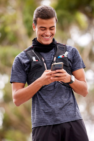 Fitness, man and phone with smile for social media, communication or chatting in nature. Happy active male smiling on mobile smartphone for chat, texting or networking after outdoor workout exerciseの写真素材