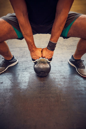 Push it to the limit. an unrecognizable young man working out with a kettle bell in the gym.の写真素材