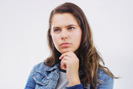 Shes left with a tough decision. Studio shot of a young woman looking thoughtful against a gray background.の写真素材