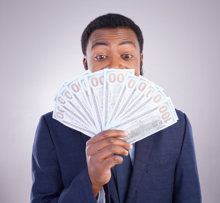 Eyes, cash and investment with a business black man in studio on a gray background as a lottery winner. Money, accounting and finance with a male employee holding dollar bills for the economyの写真素材