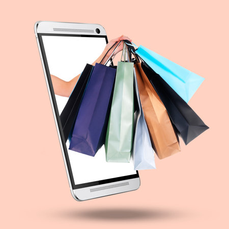 Hands, phone and screen on mockup with shopping bags for purchase, advertising or marketing against a studio background. Hand of shopper with gifts on mobile smartphone display for online ecommerceの写真素材