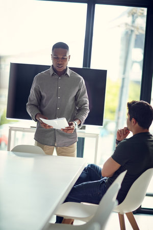 Ive brought some numbers to share with you. two young businessmen going over paperwork together in a modern office.の写真素材
