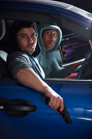 Hacking is a crime. two armed young hackers using a laptop in a car.の写真素材