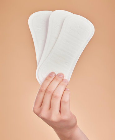 Hand, sanitary pads and period with a woman in studio on a brown background for female hygiene or care. Lifestyle, and gynecology with a female holding a feminine product for her menstrual cycleの写真素材
