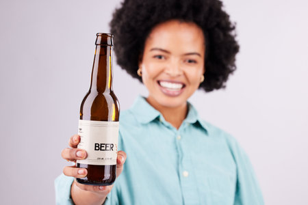 Hand, beer and advertising with a black woman in studio on a gray background for alcohol promotion. Portrait, bottle and beverage with a female holding a product for celebration or congratulationsの写真素材