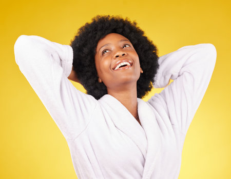 Black woman relax, bathrobe and happiness in a studio ready for luxury spa treatment for self care. Isolated, yellow background and happy young female with a smile from skincare and wellnessの写真素材