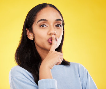 Secret, portrait and woman with finger on lips in studio, yellow background and privacy sign. Face of female model, silence and shush for quiet, gossip and whisper emoji for confidential mystery newsの写真素材