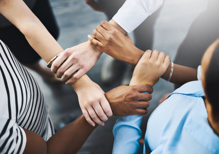 Keep close to those that continuously motivate you. High angle shot of a group of businesspeople holding one anothers wrists in a circular formation.の写真素材