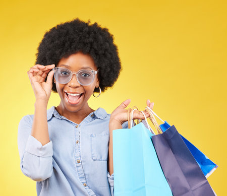 Fashion, portrait and black woman with shopping bags, smile and excited for sale in studio on yellow background. Face, shopper and girl customer cheerful after boutique, retail or store discountの写真素材
