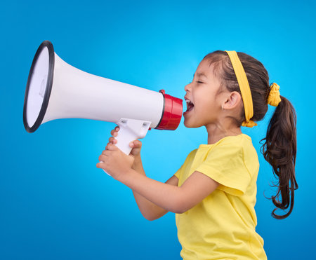 Communication, shout and child with megaphone for news, opinion and announcement on blue background. Talking, speaking mockup and young girl with loudspeaker for voice, scream and attention in studioの写真素材
