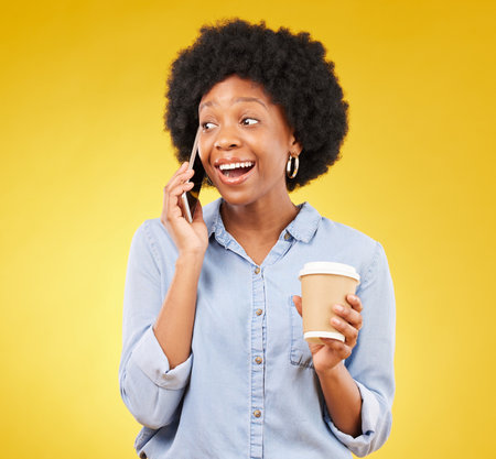 Phone call, happy and black woman with coffee in studio, smile and listening on yellow background. Smartphone, conversation and girl with tea surprised, joke and humor while enjoying speaking onlineの写真素材