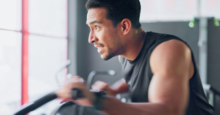 Strong man, gym air bike and cardio training for exercise, workout and strong body, muscle and power in fitness club. Happy, healthy and young bodybuilder cycling fast on stationary bicycle machineの写真素材
